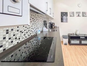 A modern kitchen with a black induction cooktop, a stainless steel sink, and a tiled backsplash. - GuestReady - Pico del torreon (El Puerto de Santa María)