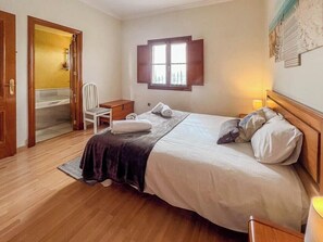 Ein Hotelzimmer mit Bett, Sessel, Nachttisch, Fenster und Tür zu einem Badezimmer.