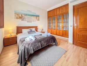 A bedroom with a bed, nightstands, a wooden wardrobe, and a beach-themed wall art. - GuestReady - Pico del torreon (El Puerto de Santa María)