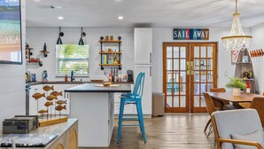 Uma cozinha moderna com uma ilha central, uma área de jantar com a placa 'Sail Away' e vista para o exterior.