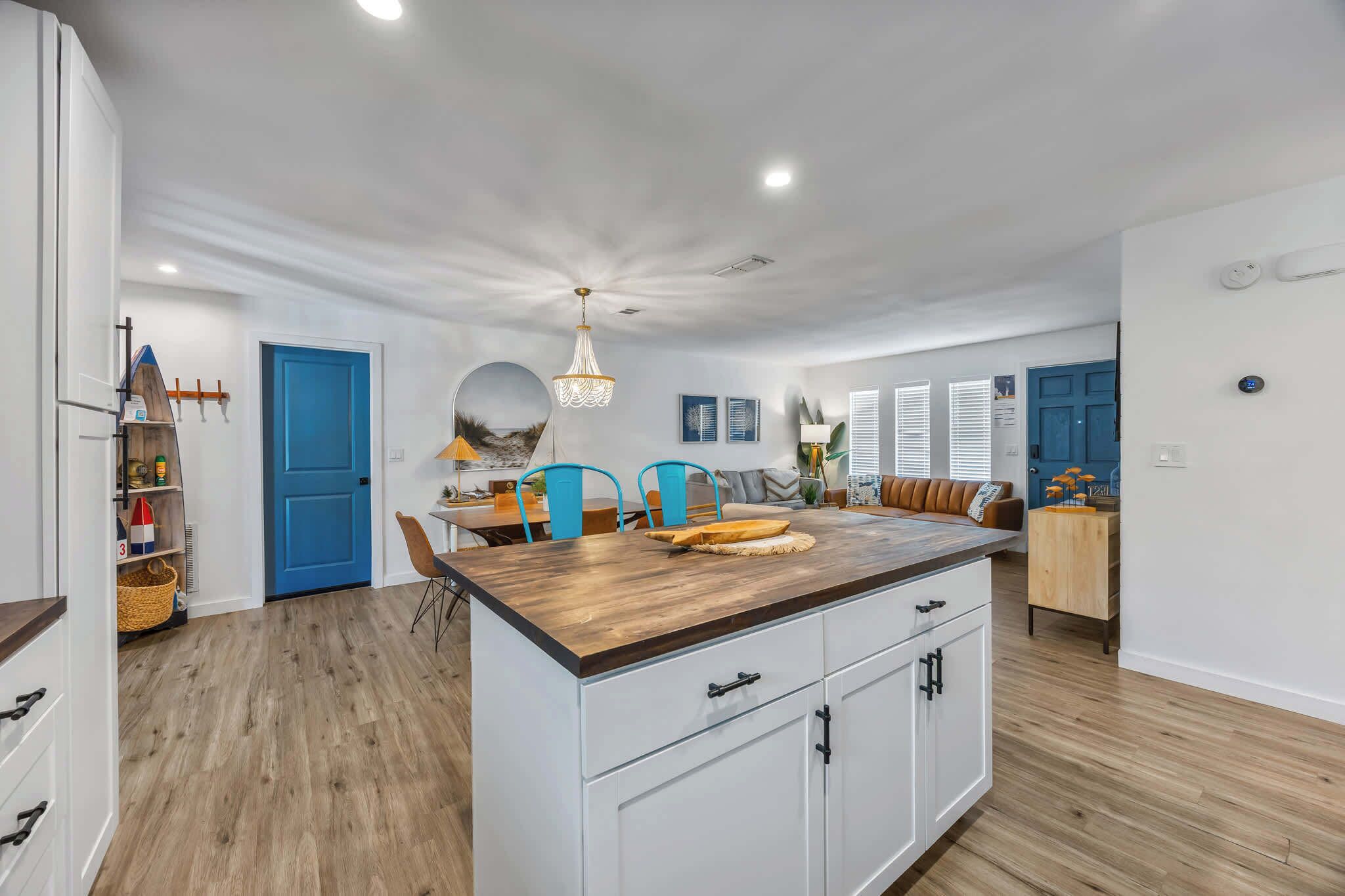 A modern kitchen with a central island, wooden flooring, and a blue door.