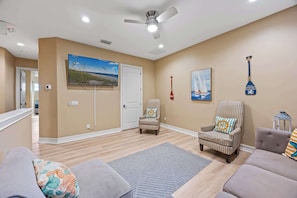 A living room with a flat-screen TV, a ceiling fan, and a painting of sailboats. - Group-Friendly 5BR/4.5BA with Private Yard (Indian Harbour Beach)