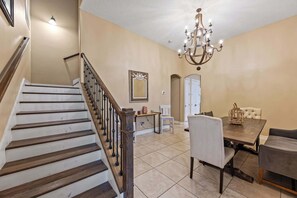 A dining area with a chandelier, a staircase, and a white chair. - Group-Friendly 5BR/4.5BA with Private Yard (Indian Harbour Beach)