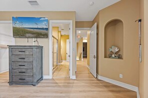 A hallway with a wooden dresser, a painting of a beach, and an arched doorway. - Group-Friendly 5BR/3.5BA with Private Yard (Indian Harbour Beach)