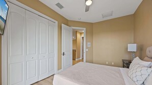 A bedroom with a bed, a nightstand, a lamp, a ceiling fan, and a door leading to another room. - Group-Friendly 5BR/4.5BA with Private Yard (Indian Harbour Beach)