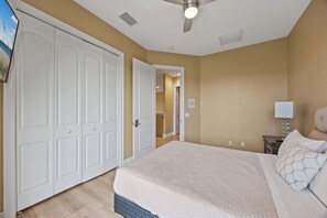 A bedroom with a bed, a nightstand, a lamp, a ceiling fan, and a door leading to another room. - Group-Friendly 5BR/4.5BA with Private Yard (Indian Harbour Beach)