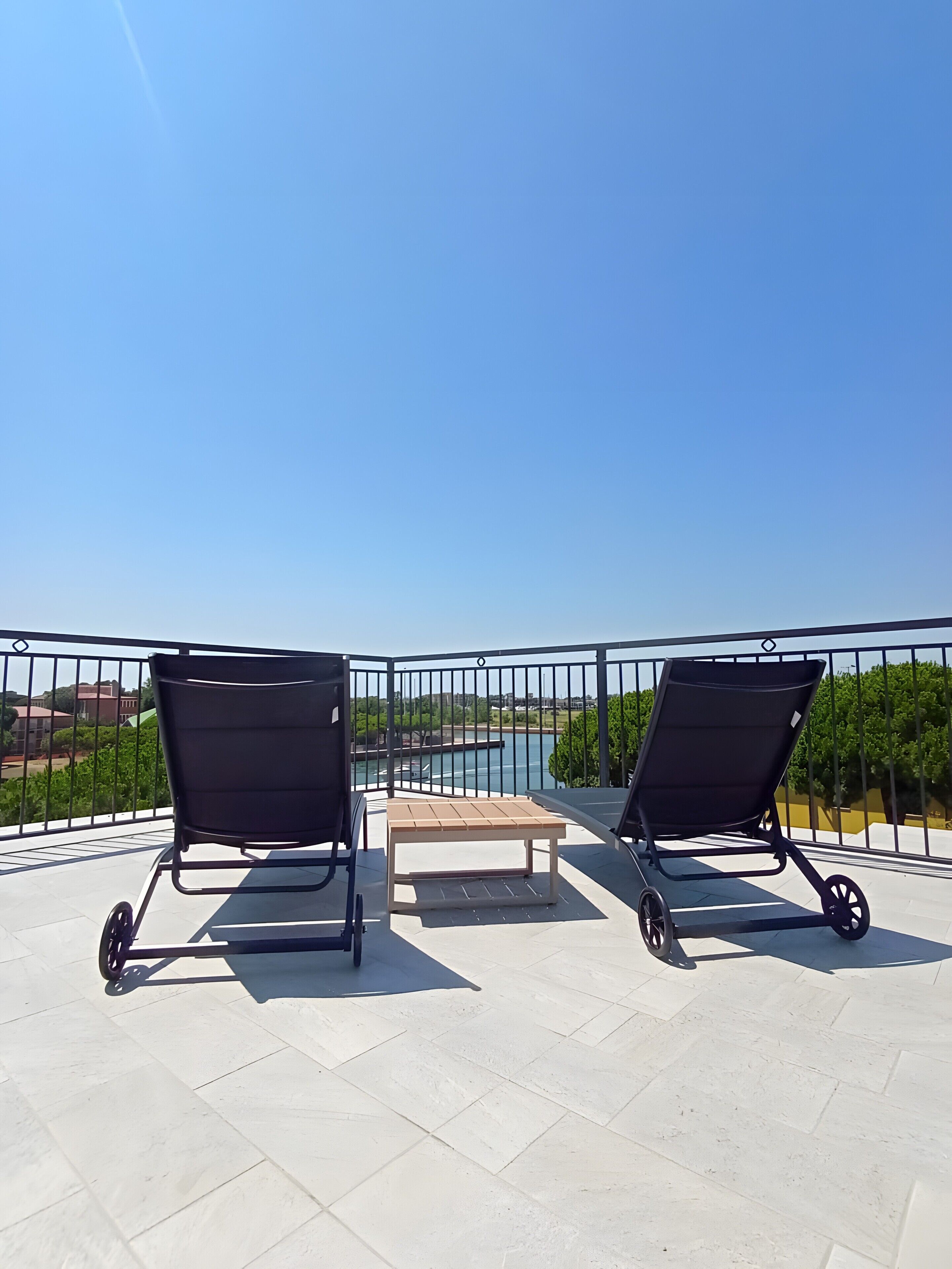 Un balcon avec deux fauteuils noirs et une petite table, donnant sur une étendue d’eau et sur de la verdure.