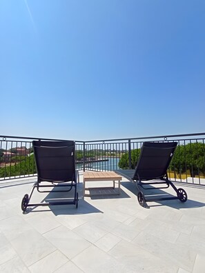 Een balkon met twee zwarte loungestoelen en een kleine tafel, met uitzicht op water en groen.
