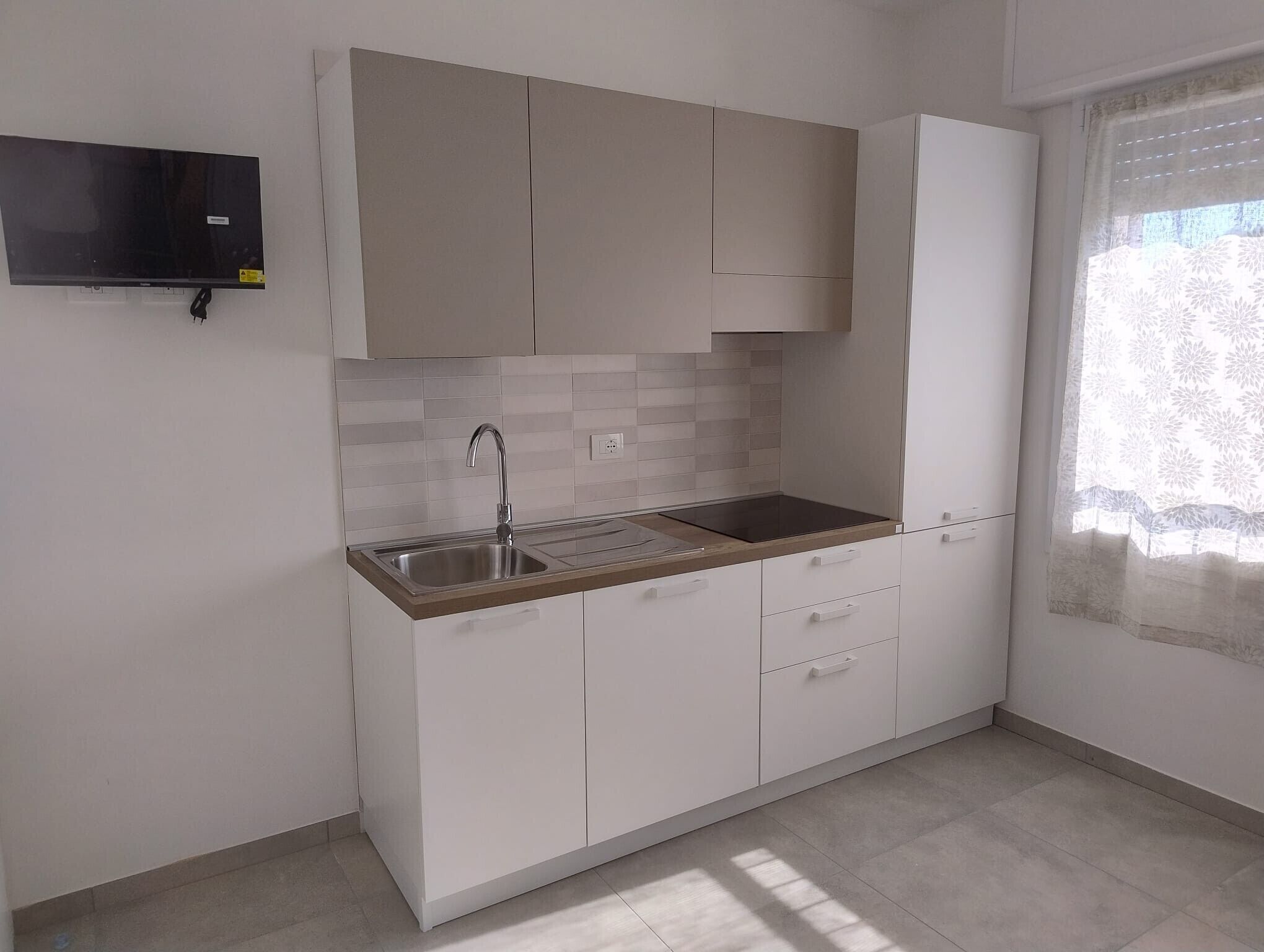 Uma cozinha moderna com armários brancos, uma pia de aço inoxidável e um forno embutido.