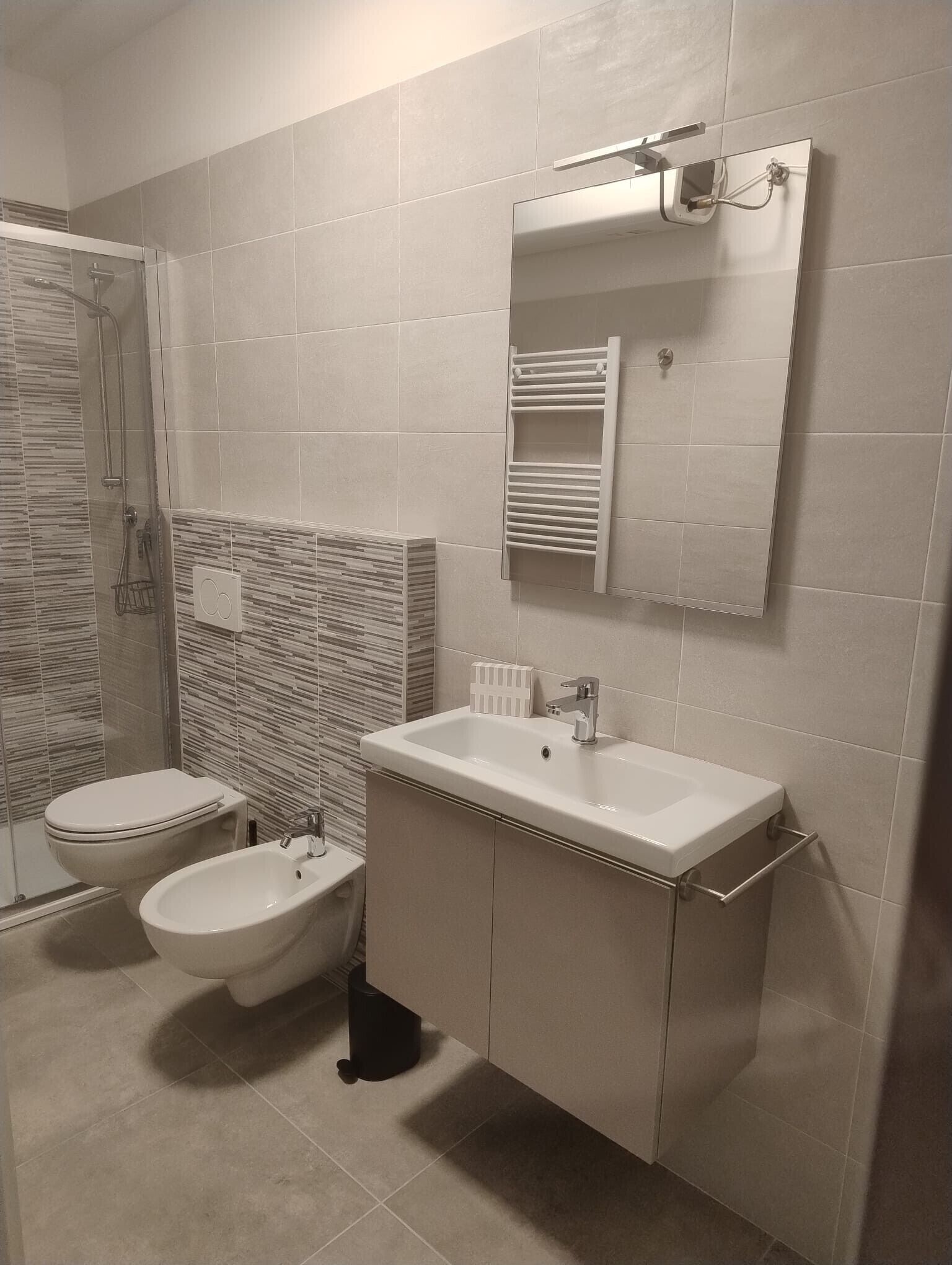 Een badkamer met een douche, toilet, bidet en een wastafel met spiegel erboven.