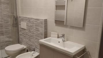 Een badkamer met een douche, toilet, bidet en een wastafel met spiegel erboven.