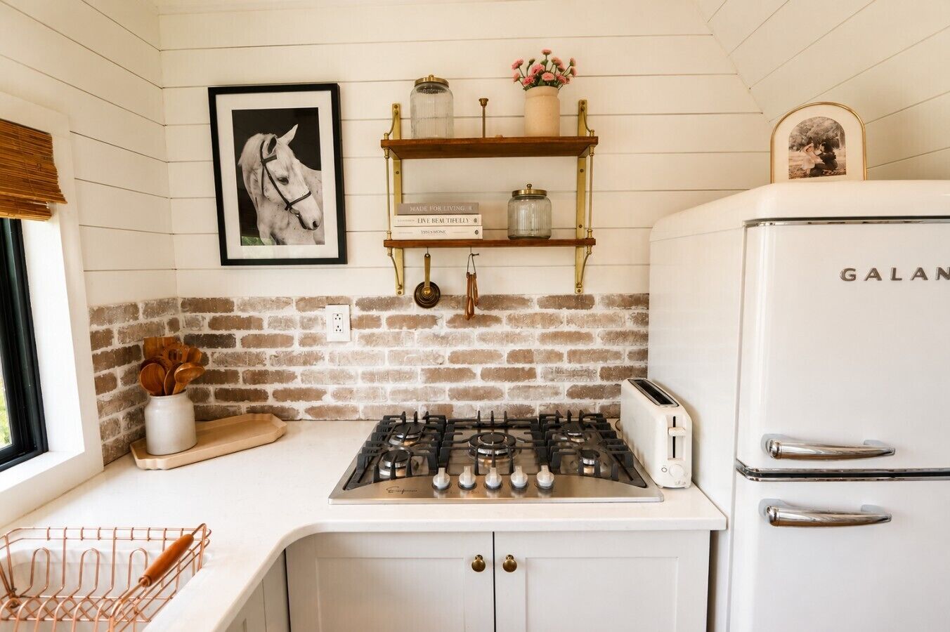 A kitchen with a gas stove, a white refrigerator, and a brick wall.