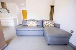 Un salon moderne avec un canapé d’angle gris et des coussins assortis, un meuble encastré blanc et une porte en bois.