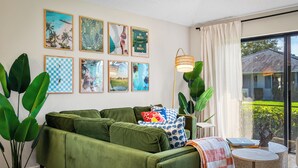 Ein grünes Sofa mit Kissen, ein kleiner runder Tisch mit Büchern und eine Lampe.
