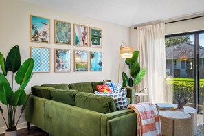Ein grünes Sofa mit Kissen, ein kleiner runder Tisch mit Büchern und eine Lampe.