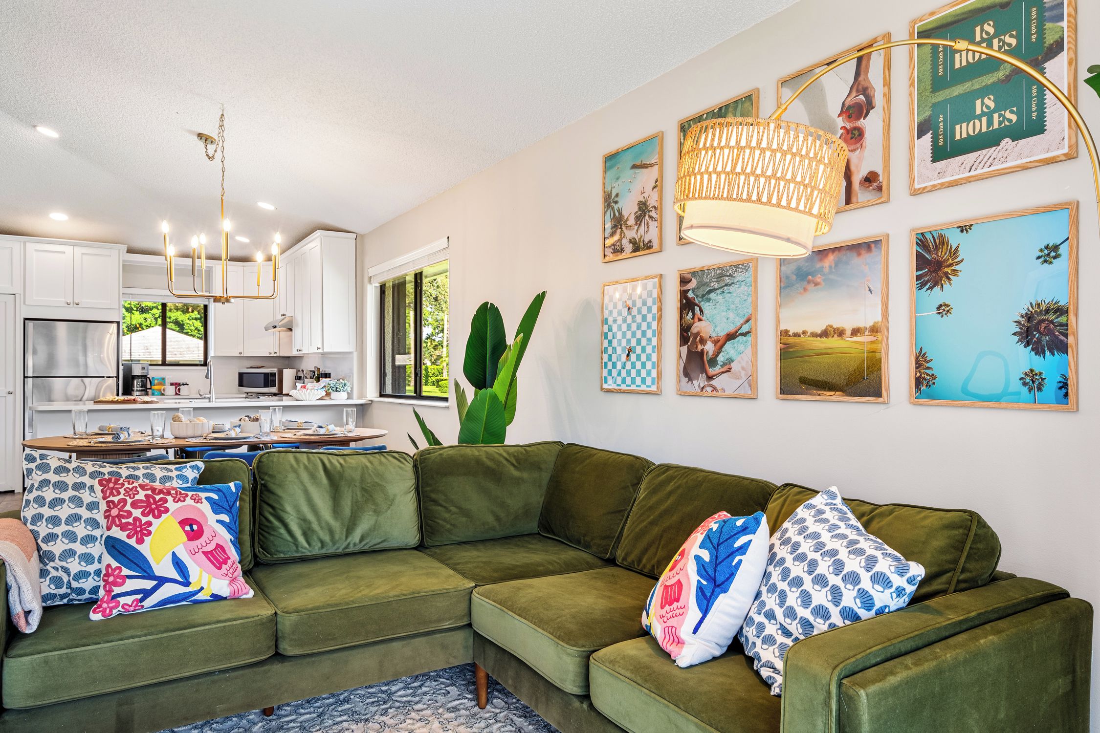 Una sala de estar moderna con un sofá seccional verde, un comedor con mesa y sillas, y una cocina con armarios blancos.