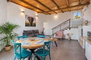 Ein Essbereich mit einem Holztisch und türkisfarbenen Stühlen, einem grauen Sofa und einer Treppe, die in eine obere Ebene führt.