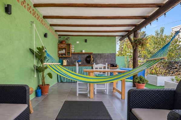 Ein überdachter Patio-Bereich mit einer Hängematte, Sitzmöbeln im Freien, einem Esstisch und einer Küchenzeile.