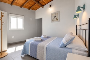Un dormitori amb un llit, una finestra, una làmpada penjada a la paret i una porta.
