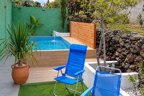 Una piscina amb un pont de fusta, una cadira blava i una planta en test.