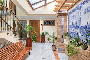 A spacious indoor area with a wooden bench, potted plants, a tiled wall with a cityscape design, and a staircase with a glass ceiling. - GuestReady - Urban Suite City Center (La Laguna)