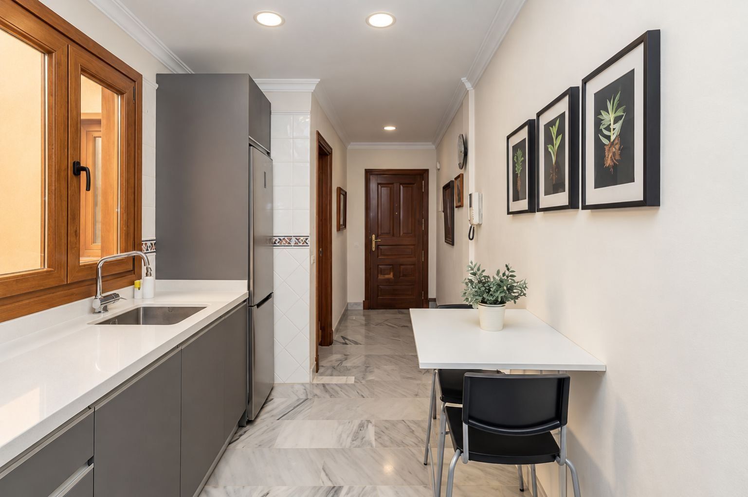 Una cocina con piso de mármol, un refrigerador, un lavamanos y una zona de comedor con sillas y una mesa.