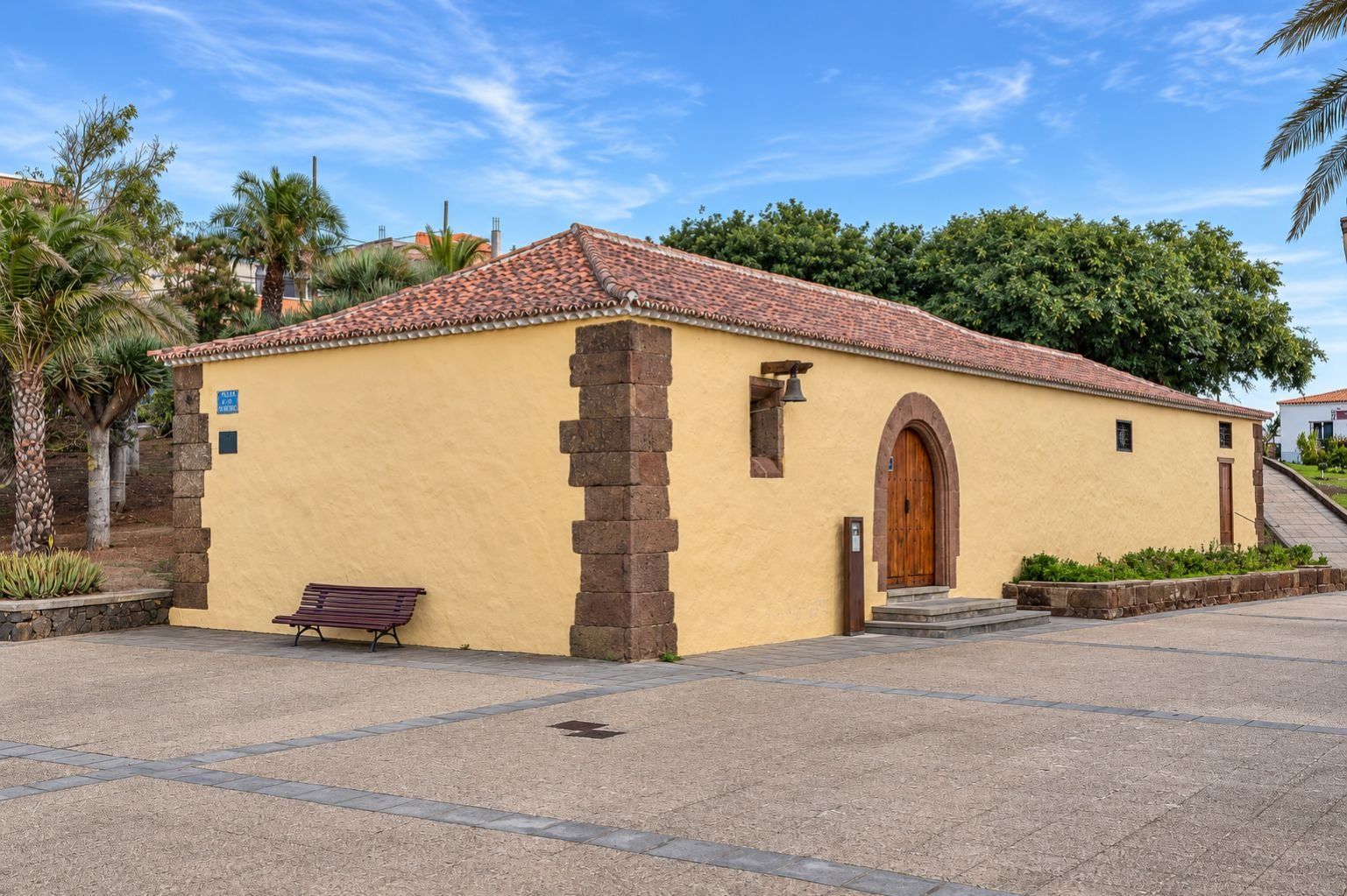 Un pequeño edificio con techo de tejas, puerta de madera y un banco en el exterior.