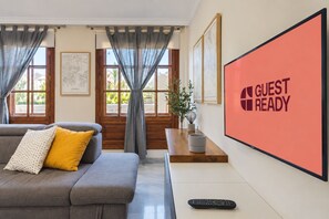 A modern living room with a grey sofa, a yellow pillow, a remote control, and a 'GUEST READY' sign on the wall. - GuestReady - Urban Suite City Center (La Laguna)
