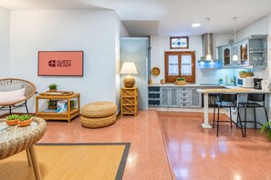 A modern kitchen with a dining area, a wicker chair, a small table with a book, and a 'GUEST READY' sign. - GuestReady - Plaza Corredera Modern Comfort (Córdoba)
