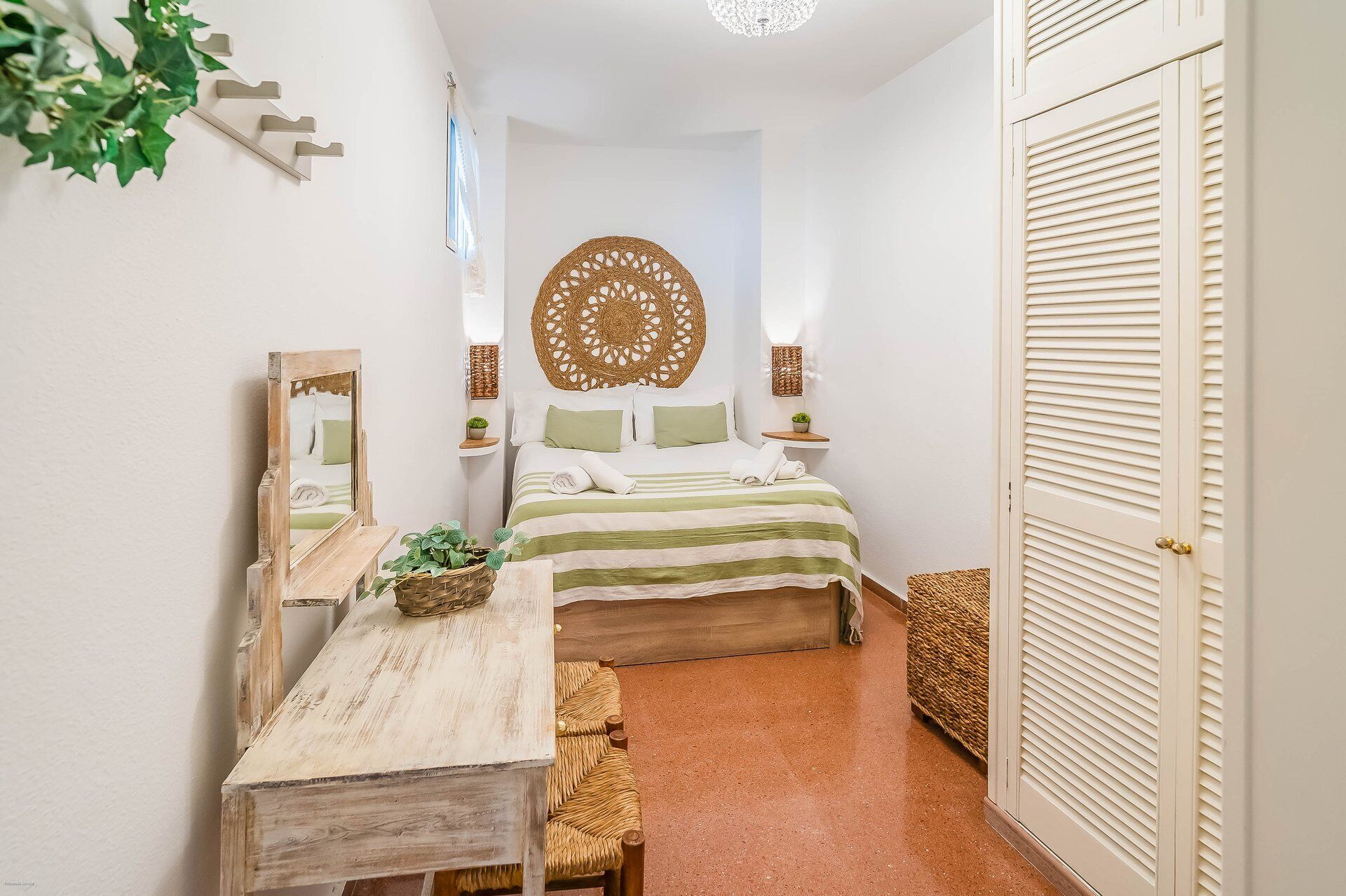 Ein Schlafzimmer mit einem Bett, Nachttischen, einem Spiegel, einer Hängeleuchte und einer Tür.