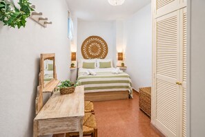 A bedroom with a bed, bedside tables, a mirror, a hanging plant, and a woven wall hanging. - GuestReady - Plaza Corredera Modern Comfort (Córdoba)