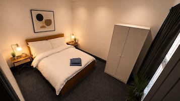 A hotel room with a bed, bedside tables, a wardrobe, a framed artwork, and a ceiling light fixture.