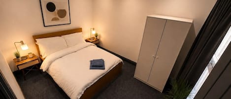 Una habitación de hotel con cama, mesitas de noche, armario, una obra de arte enmarcada y una lámpara en el techo.