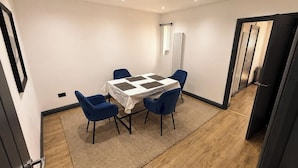 Ein kleiner, gut beleuchteter Raum mit einem Tisch und vier Stühlen, einer Deckenleuchte und einer Tür zu einem anderen Zimmer.