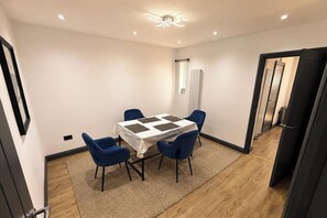 A small, well-lit room with a table and four chairs, a ceiling light, and a door leading to another room. - Tranquil Haven in Hornchurch - 3 bed House (Hornchurch)