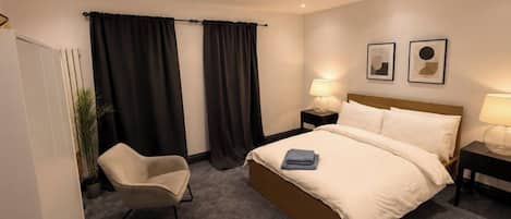 A hotel room with a bed, a chair, a nightstand, and a lamp.