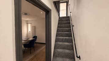 A staircase with carpeted steps and a handrail, leading to a room with a desk and chairs.