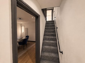 A staircase with carpeted steps and a handrail, leading to a room with a desk and chairs.
