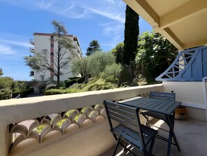 Un balcon avec une table et des chaises, donnant sur un immeuble et sur de la verdure.