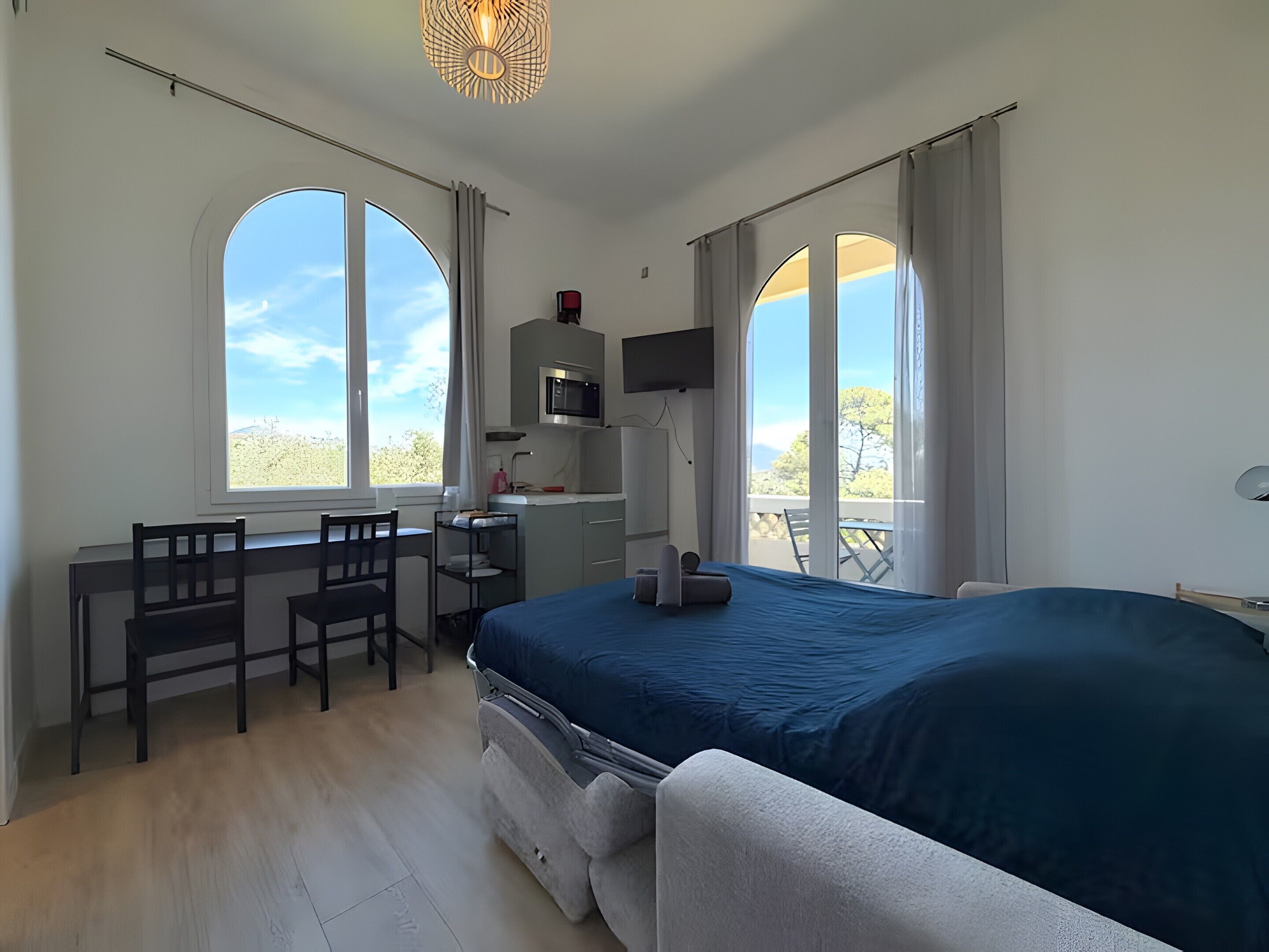 A bedroom with a bed, a desk with a chair, a television, and large windows.