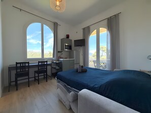 Ein Schlafzimmer mit einem Bett, einem Schreibtisch mit Stuhl, einem Fernseher und großen Fenstern.