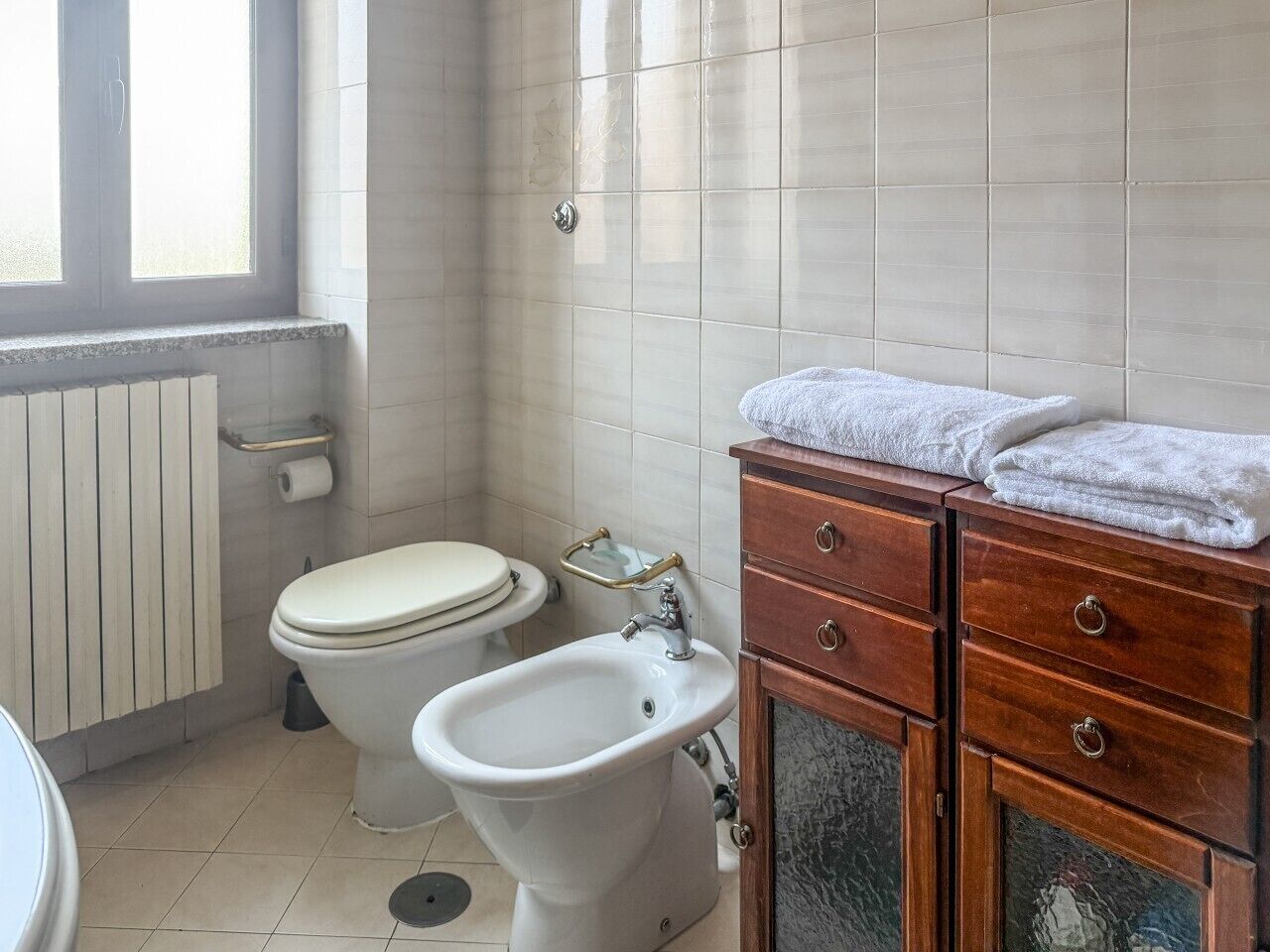 Un bagno con un water, un bidet e un mobile contenitore in legno con cassetti.