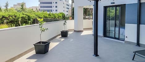 A rooftop terrace with potted plants, a glass door entrance, and a view of surrounding buildings.