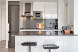A modern kitchen with a stainless steel refrigerator, a microwave, and a built-in oven. There are two bar stools and a wooden cutting board on the counter. - GuestReady - Marbella with terrace and pool (Marbella)