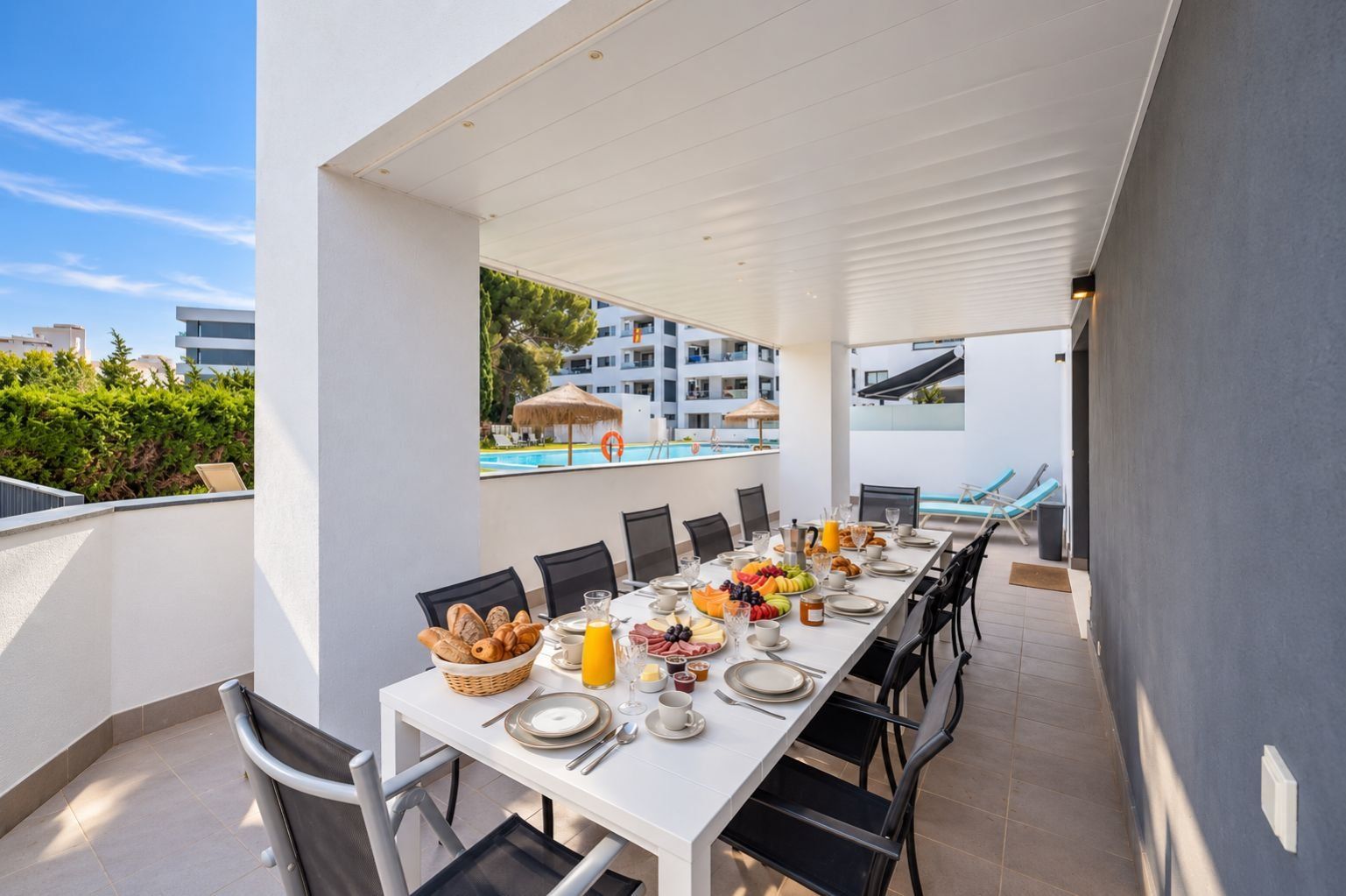 A dining area with a table set for breakfast, overlooking a pool and a building.
