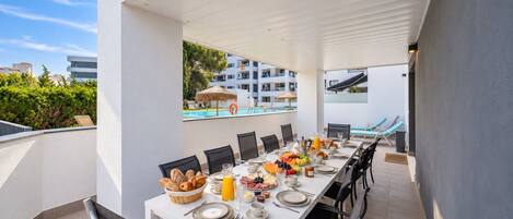 A dining area with a table set for breakfast, overlooking a pool and a building.