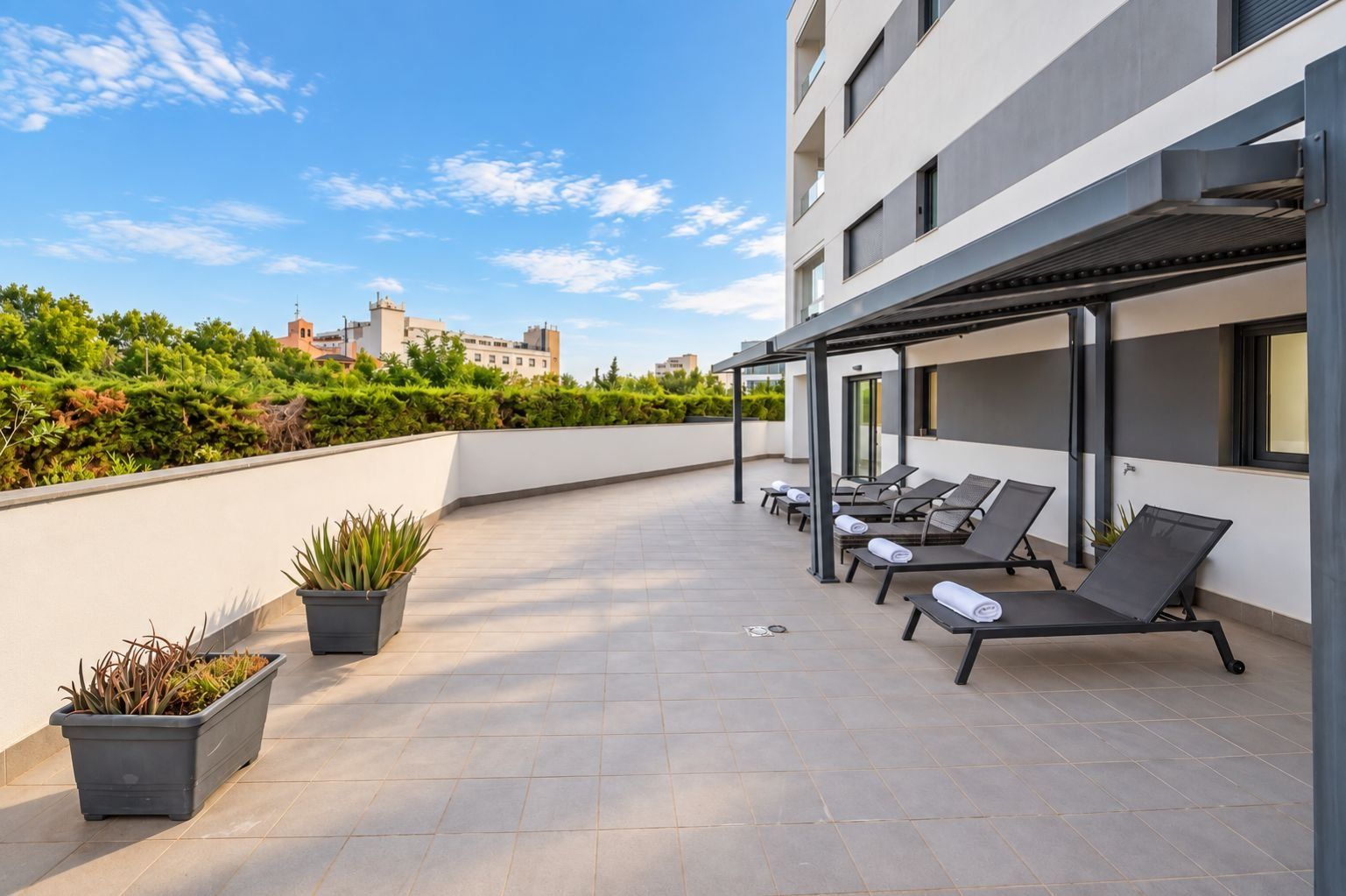 Una terraza en la azotea con tumbonas, plantas en macetas y vistas de la ciudad.