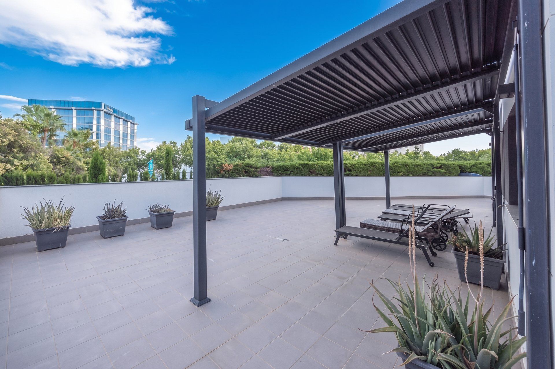 A rooftop patio with a pergola, seating, and potted plants.