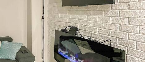 A modern living room with a flat-screen TV mounted above a white brick fireplace, a sofa with cushions, and a floor lamp.