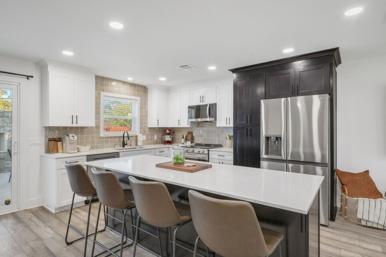 A modern kitchen with white cabinetry, a stainless steel refrigerator, and a central island with bar stools.